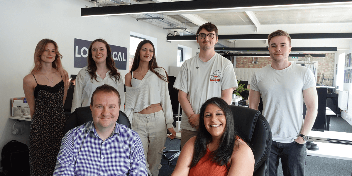 Our team, LoudLocal, facing a camera together. Five people are stood behind in the back whilst two are sat down in chairs at the front, all smiling. 