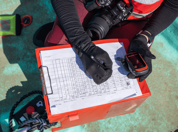 A marine biologist collecting data and recording it whilst on board a boat