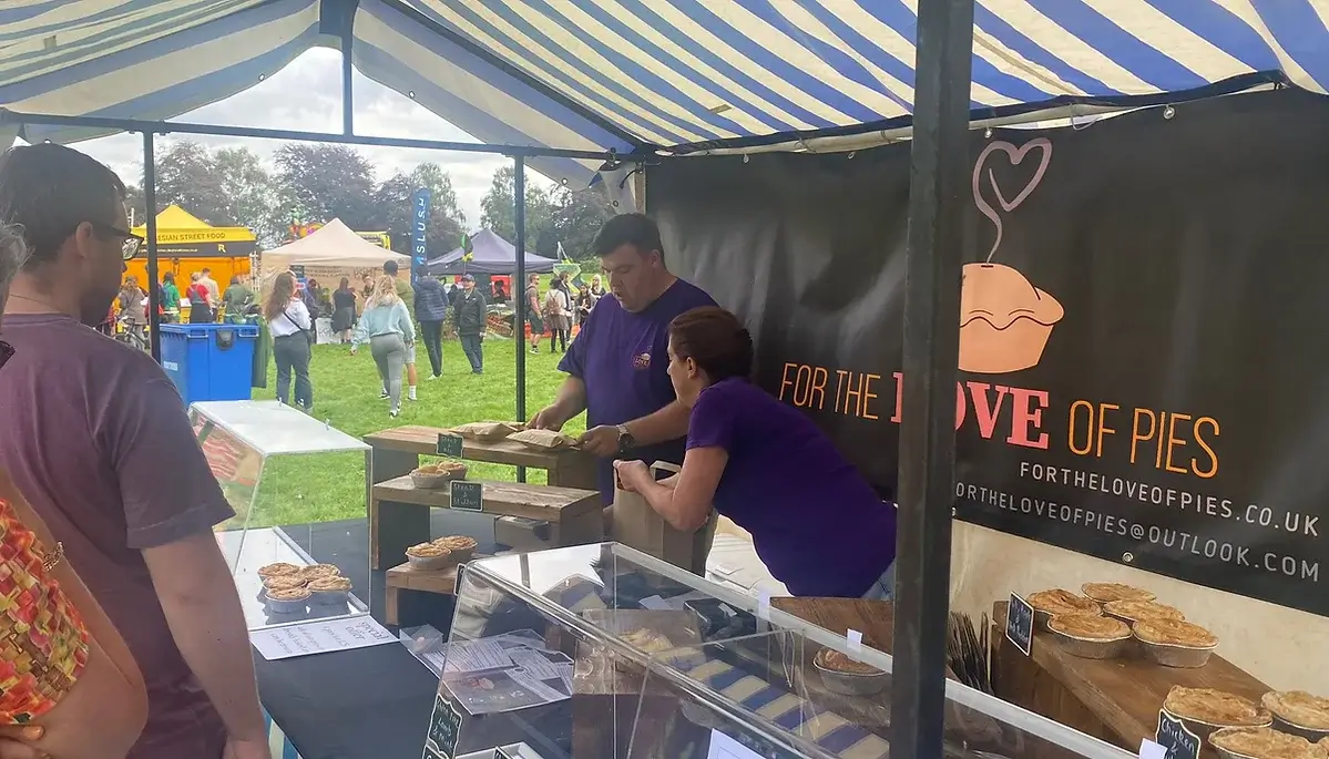 An image of the For the love of pies team selling pies at a local food festival stand with the logo designed by LoudLocal on the banner behind